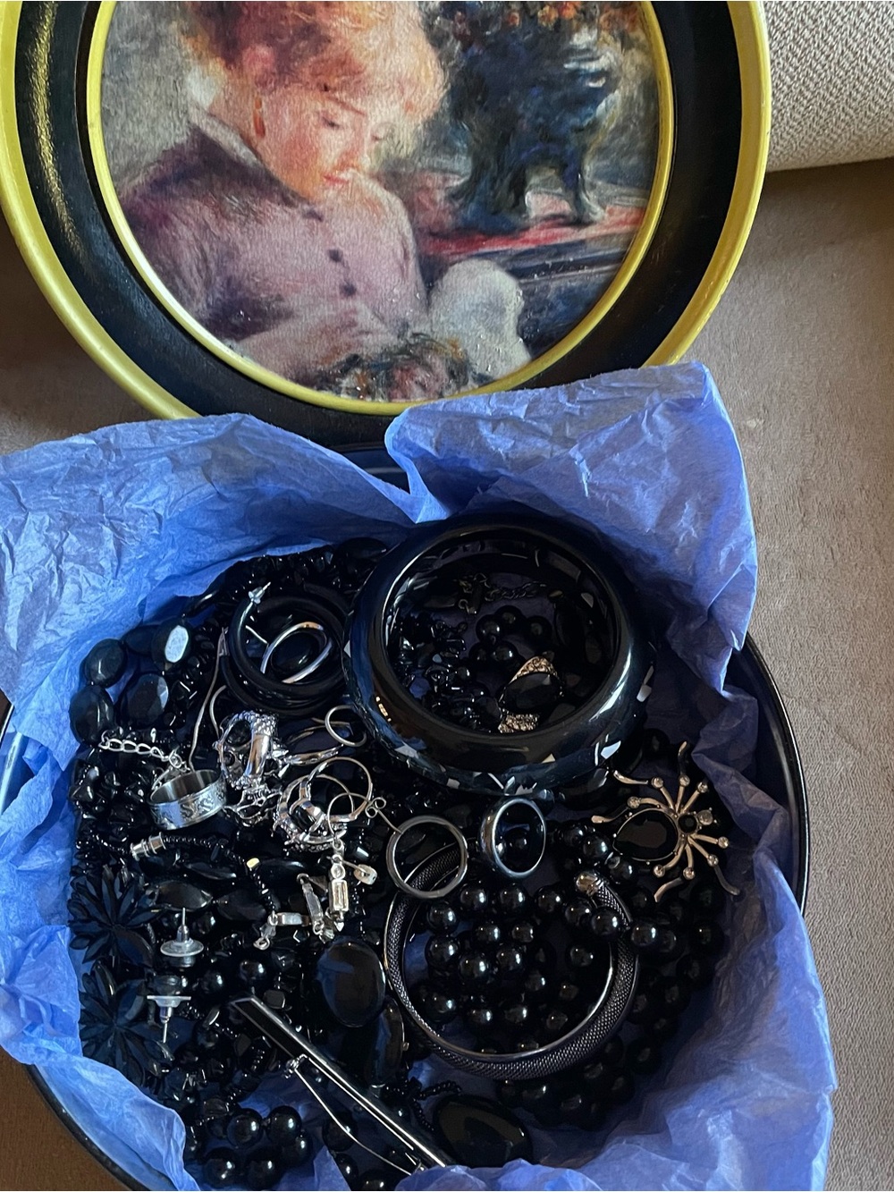 Bundle of black tone fashion jewelry in a vintage tin box .